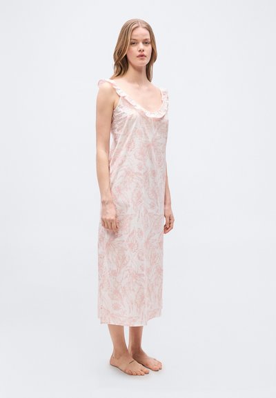 Γυναίκα με φόρεμα χωρίς μανίκια, μέχρι τον αστράγαλο, με ροζ λουλουδένιο σχέδιο και ζαρωτή λαιμόκοψη, όρθια ξυπόλυτη μπροστά σε απλό φόντο.