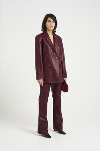 Burgundy leather suit with crocodile texture, featuring a double-breasted blazer and flared pants. Clutch bag with bead accents.