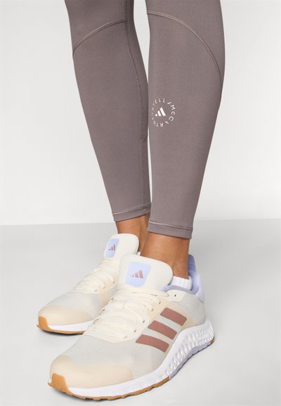 Light beige Adidas running shoes with brown stripes worn with taupe leggings featuring a circular logo near the calf.