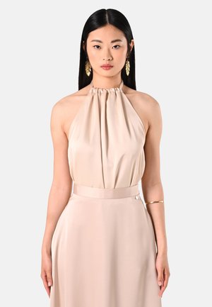 Beige halter neck dress with a gathered neckline, smooth satin texture, and a fitted waist. Gold bangle on the arm adds a metallic accent.