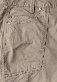Pantalons beige clair avec une finition texturée, deux boutons ronds en métal et des coutures contrastées sur la poche avant et les coutures.