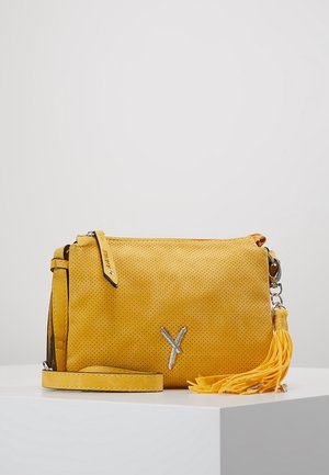 Bolso bandolera amarillo perforado con logo Y plateado, correa a juego y adorno de borla amarilla sobre superficie blanca con fondo gris.