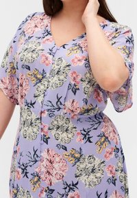 Kortärmad, V-ringad klänning i lavendelfärgad tyg med blommönster. Har knappar framtill och djärva rosa och gula blomdesigns.