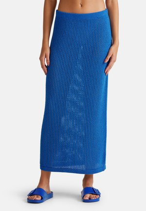 Blaue Netz-Maxi-Rock mit breitem Bund, der ein lockeres Strickmuster aufweist. Kombiniert mit passenden blauen Schlüpfrsandalen.