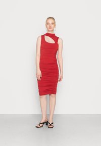 Vestido bodycon vermelho com recorte lateral, apresentando detalhes franzidos por toda a parte. Tecido suave e elástico com silhueta justa. Sapatos de salto pretos com tiras.