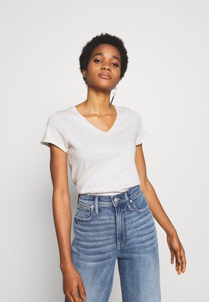 Light gray V-neck t-shirt with short sleeves, paired with high-waisted blue jeans featuring horizontal stitching details and a smooth texture.