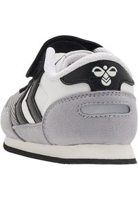 Graue und weiße Sneaker mit einem Design aus Wildleder und Mesh. Verfügt über einen Klettverschluss, schwarze Akzente und ein Logo auf der Rückseite. Niedrigprofilsohle.
