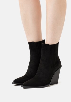 Zwarte suède enkellaarsjes met een spitse neus en een sleehak, voorzien van geribbelde elastische zijpanelen voor gemakkelijk aan- en uittrekken. Overal een gladde textuur.