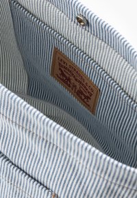 Wnętrze torby z denimu w niebiesko-białe paski z skórzaną metką z napisem „Levi Strauss & Co.” oraz mosiężnym zatrzaskiem.