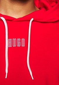 Sudadera roja hecha de un tejido suave, con un cordón blanco y un logo frontal que dice "HUGO" en una fuente contorneada.