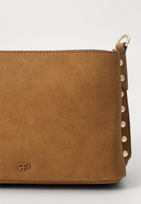 Brown suede handbag with a smooth texture, featuring cream-colored studs along one side and a logo embossed on the front.
