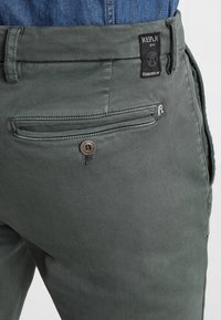 Olivově zelené bavlněné kalhoty s zadní kapsou na knoflík, prošívanými detaily a značkovou nášivkou na pásku.