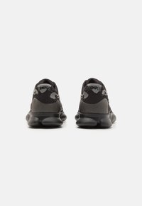 Black athletic shoes featuring a mesh upper and textured heel. Thick, rounded sole with a prominent logo on the heel.