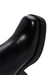Zapato de cuero negro con una parte superior suave, puntera redondeada y suela de goma texturizada. Presenta un diseño elegante con un tacón modesto.