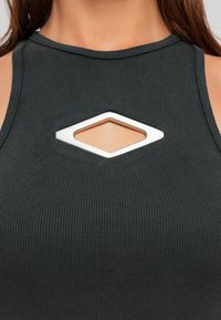 Suure plaan naisest, kes kannab musta ribaga ilma varrukateta topi, millel on rinnal diamond-kujuline lõige.