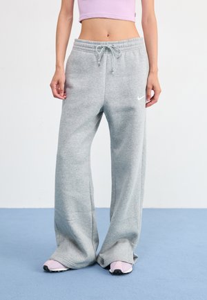 Graue Sweatpants mit lockerer Passform und Kordelzugbund. Ausgestattet mit einem kleinen weißen Logo an der Seite und pinken Sportschuhen.