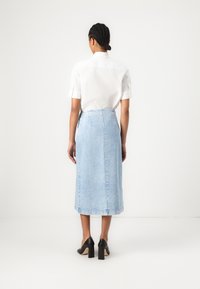 Lyseblå denimskjørt med en rett silhuett, med høy midje og subtile sømmer. Kombinert med en hvit skjorte med korte ermer og svarte hæler.