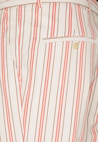 Gestreepte broek van gestructureerde stof met koraalrode en bruine verticale strepen, één achterzak en een knoopdetail.