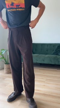 Hnedé plisované nohavice s vysokým pásom a rovnými nohavicami, vyrobené z hladkej tkaniny; v kombinácii s tmavými mokasínami.