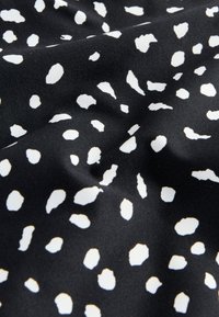 Tela negra con manchas blancas irregulares que crean un patrón estilo dálmata, mostrada con pliegues suaves y textura ligera.