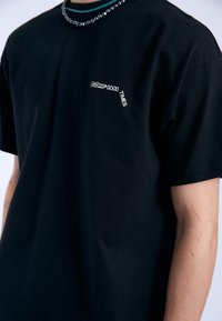 Camiseta de algodón negra con un pequeño estampado de texto blanco que dice "DREAM GOOD TIMES" en el pecho. Diseño de cuello redondo y mangas cortas.