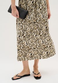 Midi sukňa s leopardím potlačou a čiernymi tenkými flip-flopami; modelka drží čiernu koženú kabelku. Hladká tkanina, splývavý dizajn.