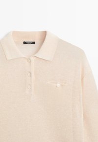 Polo en maille beige clair avec col, trois boutons sur le devant, et une petite poche avec un bouton sur la poitrine, marqué Massimo Dutti.