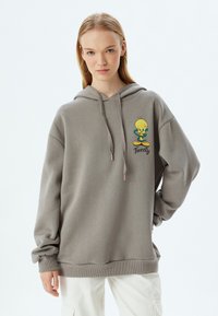 Sudadera gris con capucha, que presenta un gráfico de Pájaro Tweety de dibujos animados. Hecha de una tela suave, tiene un ajuste holgado y puños acanalados.