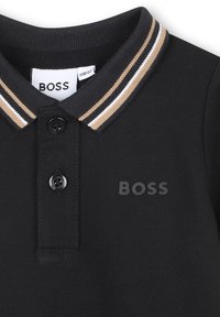 Zwarte polo met een beige en witte gestreepte kraag, twee zwarte knopen en het "BOSS" logo op de borst en het binnenlabel.