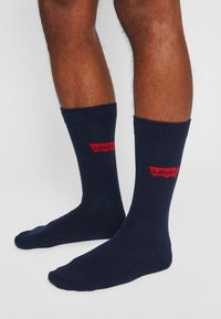 Marineblå sokker af bomuldsblanding, med ribbede manchetter og et rødt Levi's logo foran. Glat tekstur og ankellængde.