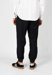 Zwarte joggingbroek met elastische boorden, een relaxte pasvorm en zijzakken, gecombineerd met zwarte sneakers met grijze accenten.