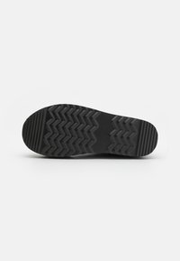 Suela de zapato de goma negra con un patrón de banda de rodadura en zigzag para tracción, textura suave y diseño de punta redondeada.