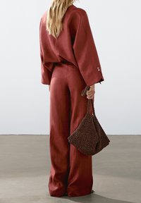 Blouse ample de couleur rouille avec manches larges, associée à un pantalon à larges jambes assorti. Accessoirisé d'un sac texturé à motif sombre.