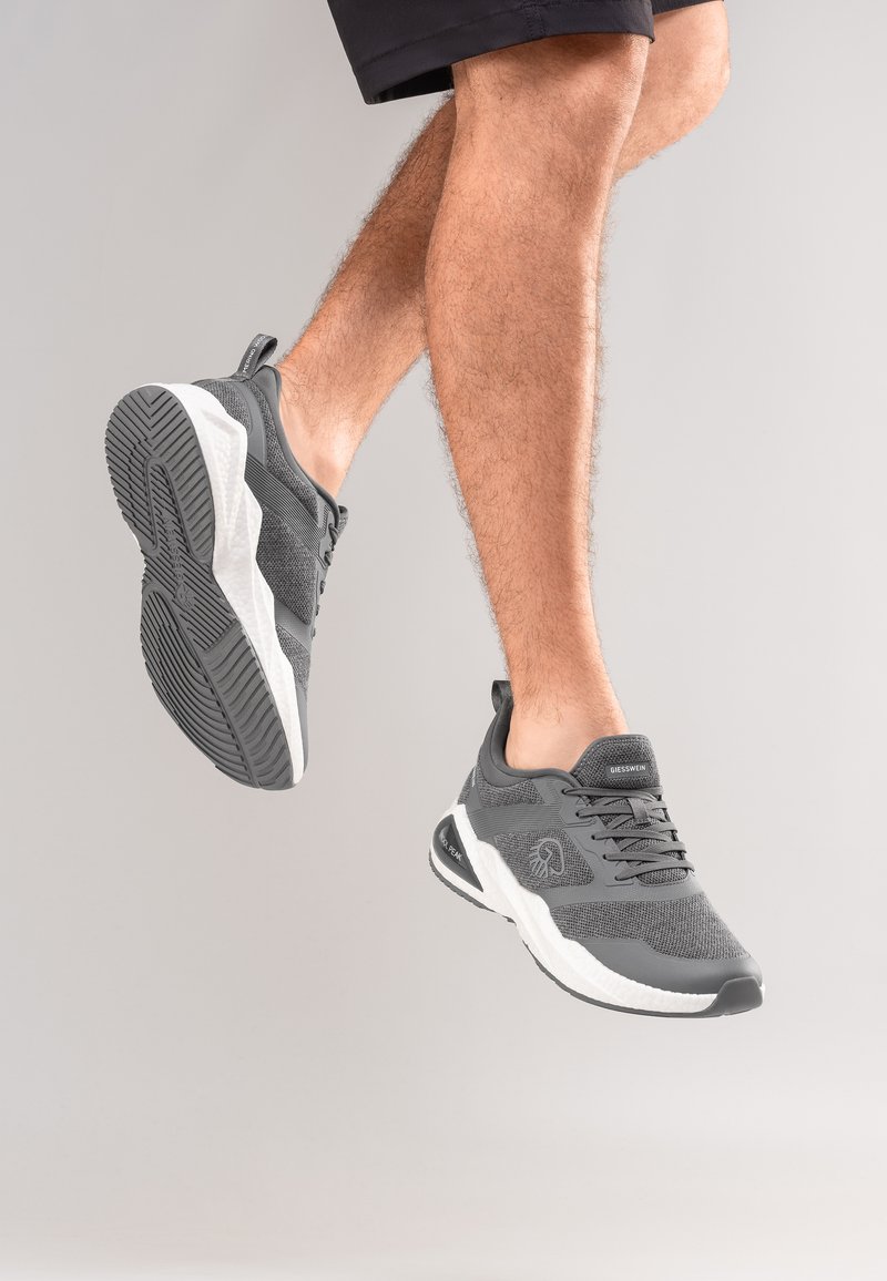 Graue Sportschuhe mit einer strukturierten Mesh-Oberfläche, gepolstertem Kragen und weißer Zwischensohle mit einer profilierten schwarzen Außensohle.