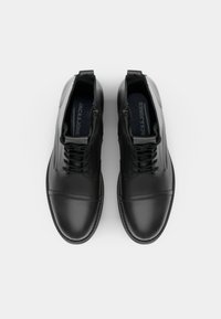 Botas de tobillo de cuero negro con cordones y cremalleras laterales, que presentan una textura suave y detalles de costura a lo largo de la puntera y los paneles laterales.