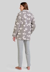 Chaqueta de forro polar en gris con manchas abstractas blancas, con cuello, combinada con pantalones ligeros de rayas grises y blancas. Textura suave, diseño casual.