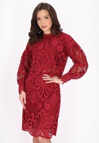 Abito rosso in pizzo con intricati motivi floreali, maniche lunghe e una vestibilità leggermente ampia con scollatura a scallop.