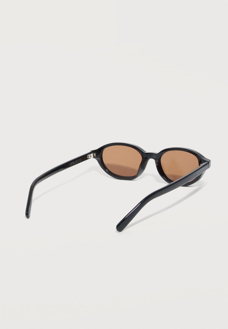 Black oval sunglasses with brown tinted lenses, resting open on a white surface.
