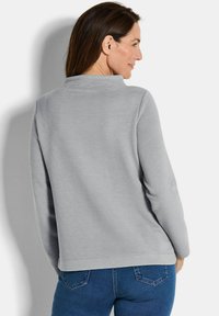 Lichtgrijze geribbelde pullover met een kraag, voorzien van lange mouwen en een rechte zoom. G gedragen met blauwe jeans. Subtiele textuurlijnen aanwezig.