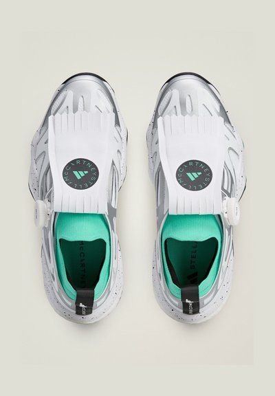 Zapatillas deportivas blancas con acentos plateados, parte superior de malla, puntera prominente, forro turquesa y detalle de logotipo circular; suela texturizada con motas.