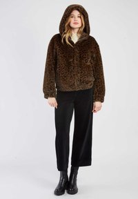 Brązowa kurtka z futra ekologicznego w leopardzim wzorze, z kapturem, zapięciem na zamek i ściągaczami przy mankietach, w zestawie z czarnymi spodniami z kordurowej tkaniny i czarnymi botkami za kostkę.
