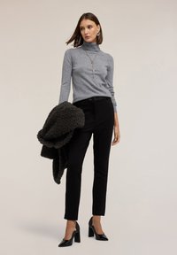 Grauer Rollkragenpullover, schwarze schmal geschnittene Hose, schwarze High Heels und ein dunkler strukturierten Schal. Schlichte Accessoires.