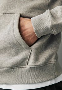 Sudadera gris con bolsillo canguro, puños acanalados y dobladillo. La tela presenta una textura suave con un patrón ligeramente jaspeado.