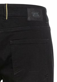 Zwarte spijkerbroek van denim met een gele stiksel op de tailleband, een vierkant merklabel aan de achterzijde en een achterzak met subtiele stiksels.