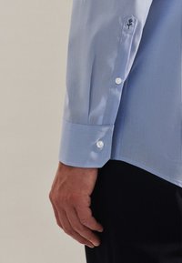 Light blue dress shirt with a smooth texture, featuring a round cuff with a white button and an embroidered floral detail on the sleeve.