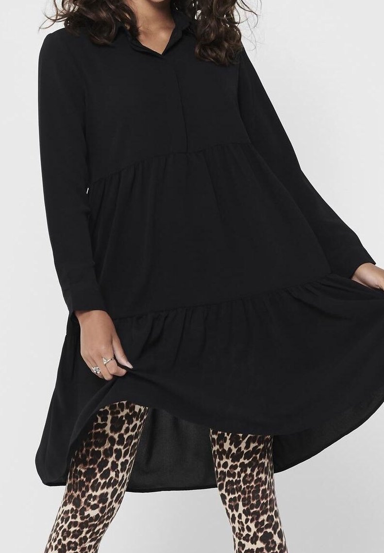Abito nero a maniche lunghe con colletto e orlo a balze, realizzato in un tessuto morbido. Indossato con leggings a stampa leopardata.