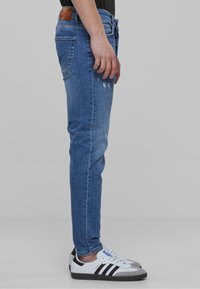 Modri jeans s slim krojem, opremljeni s poškodovanim podrobnostmi in usnjenim pasom, v kombinaciji z belimi in črnimi supergami.