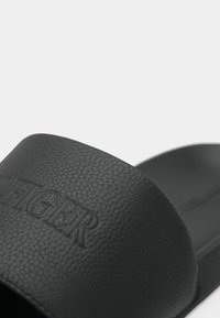 Close-up of black textured slide sandal with wide strap embossed with the word "TIGER" in capital letters.