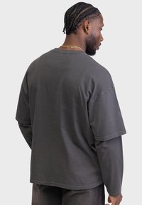 Tricou oversized gri din bumbac, cu mâneci scurte și guler rotund. Textură netedă cu detalii minime de cusătură.