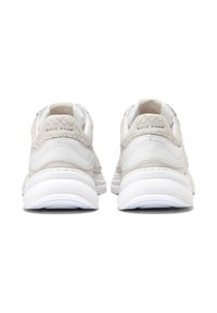 Bílé tenisky s texturovaným světle šedým akcentem, se zaobleným tvarem, polstrovaným límcem a brandingem "Cole Haan" na zadní straně.